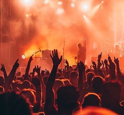 A crowd of fans cheering at a live music concert with orange stage lighting.