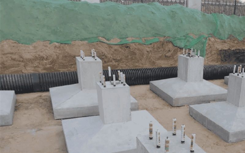 Concrete foundation blocks with exposed anchor bolts beside a corrugated pipe
